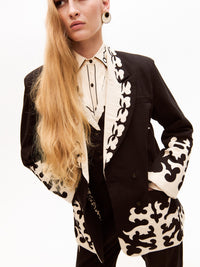 The model poses with one hand in her pocket, showcasing the elaborate embroidery on the sleeves and hem of the blazer, along with matching cream details on the pants.