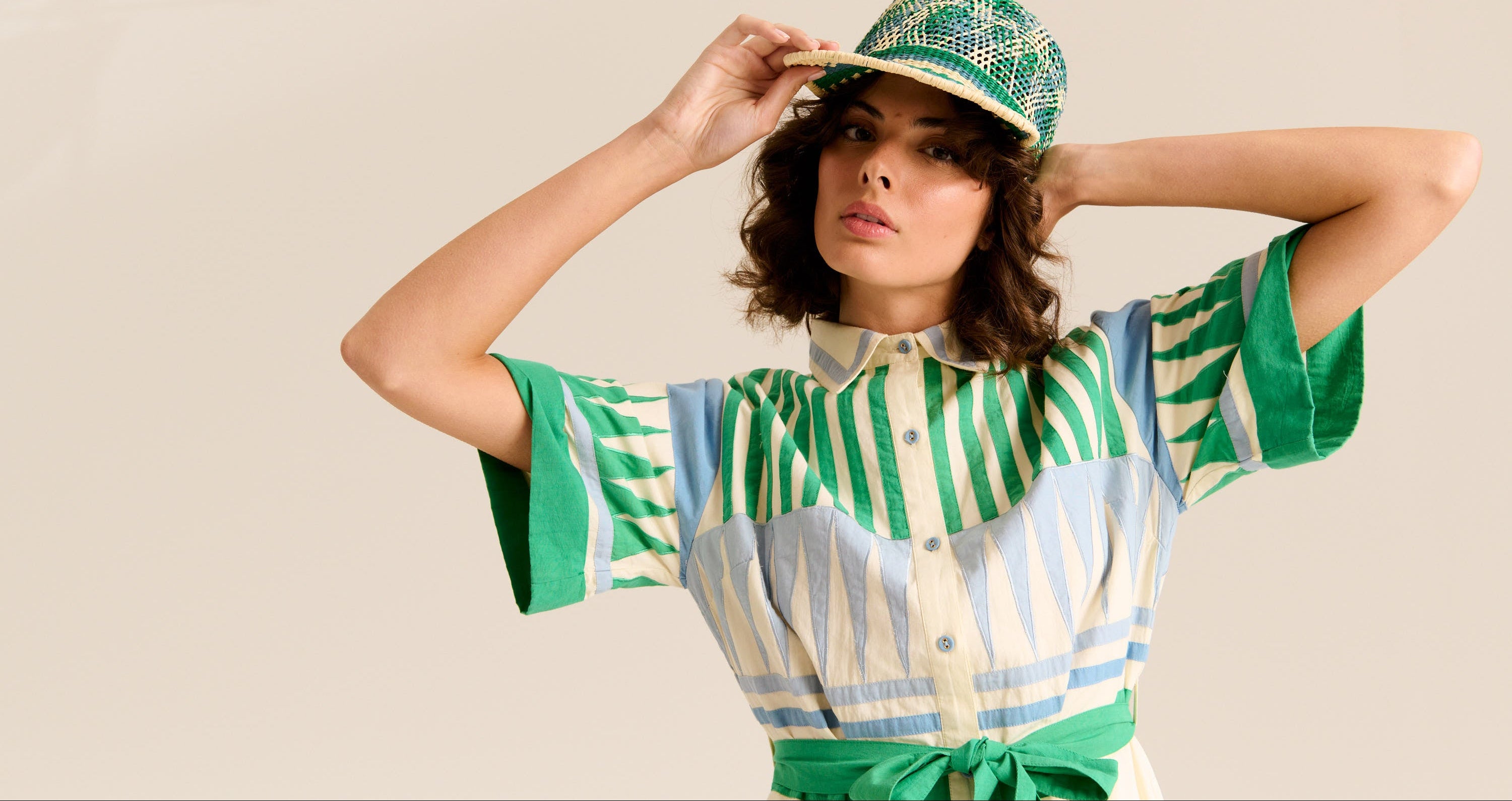 Woman wearing a green and white striped shirt with a matching cap against a beige background