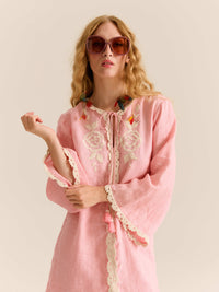 Close-up of the pink embroidered mini dress featuring lace trim, floral embroidery at the neckline, tassel ties, and the model wearing oversized sunglasses and colorful feather earrings.