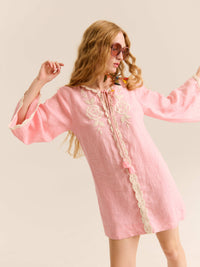 Model posing in a pink long-sleeve mini dress with lace trim and floral embroidery on the chest, styled with oversized sunglasses.
