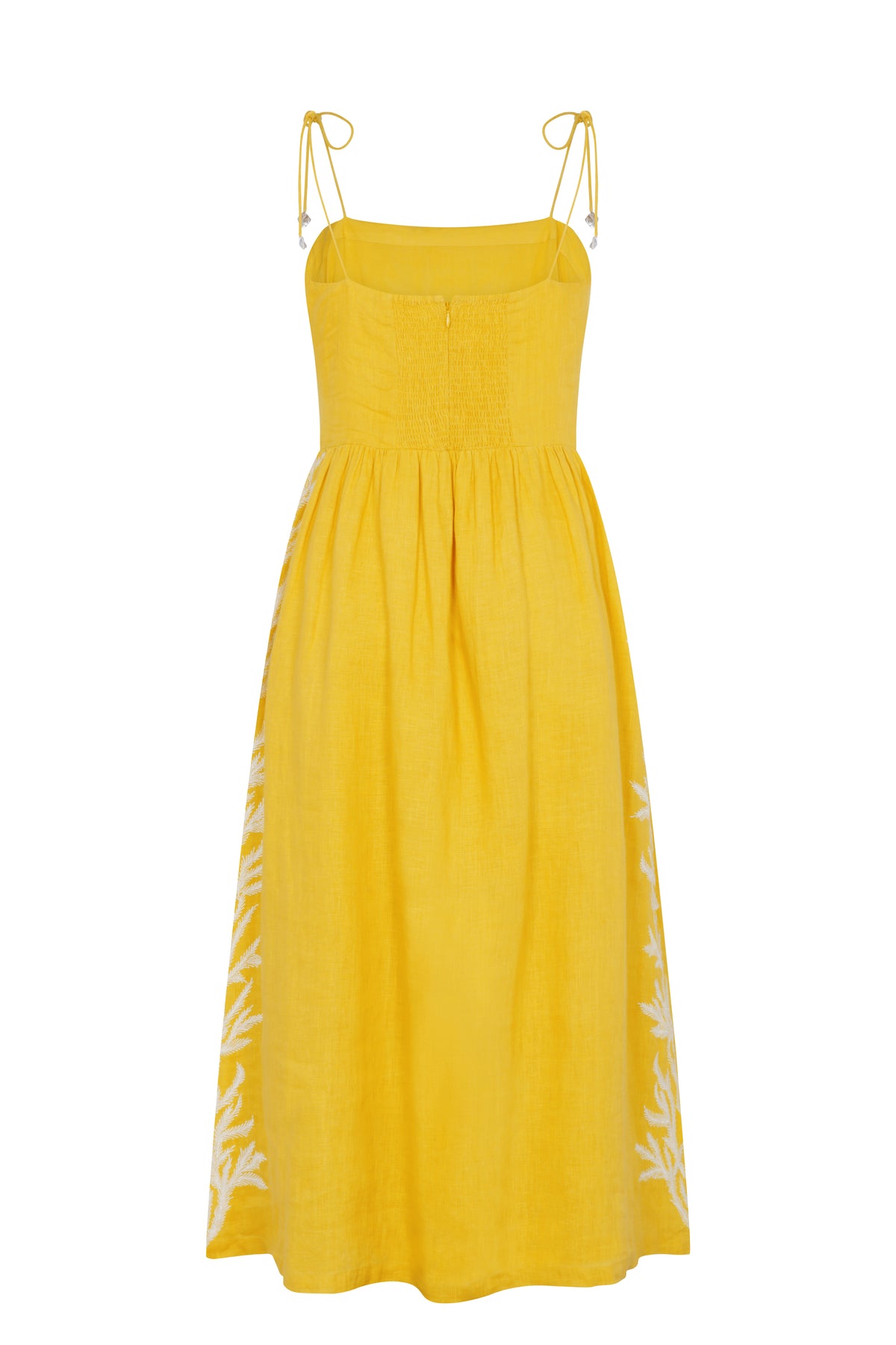 Yellow linen midi dress with adjustable shoulder ties, a smocked back bodice, and a flowing skirt. Features white embroidered botanical motifs along the sides.