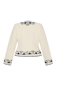 Back view of a cream tailored jacket with long sleeves and navy embroidered floral trim along the shoulders, cuffs, and hem.