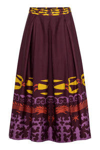 The same maroon A-line skirt shown from a slightly different angle, highlighting the structured pleats and the graphic dragon horse motif near the hem. The waistband displays woven detailing in mustard yellow and maroon, adding texture and contrast to the flowing silhouette.