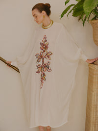 Side view of a model in an ivory embroidered kaftan dress with wide sleeves, styled with a gold necklace and earrings.