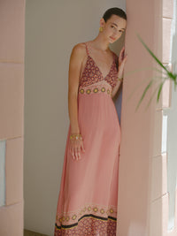 Model wearing a dusty pink V-neck maxi dress with geometric embroidered panel details.