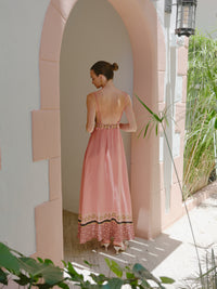 Back view of a dusty pink sleeveless maxi dress with thin straps and patterned border hem, standing under an arched walkway.