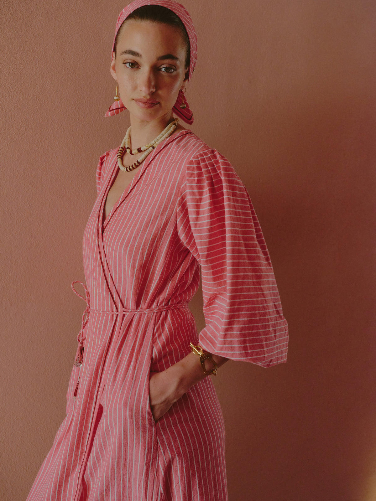 Close-up of a pink striped wrap dress with wide sleeves, styled with layered bead necklaces and gold jewelry.