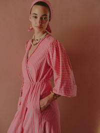Close-up of a pink striped wrap dress with wide sleeves, styled with layered bead necklaces and gold jewelry.