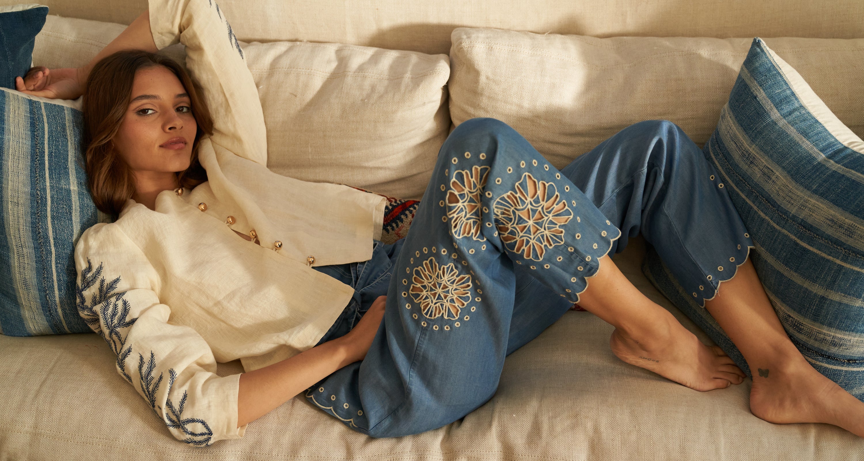 Homepage image of a girl lying down on the couch with linen white Ali Jacket & denim Carole Pants on. 