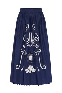 Front view of a navy blue midi skirt with a gathered waistband, full silhouette, white embroidered floral and scroll motif at the center, and a scalloped hem.