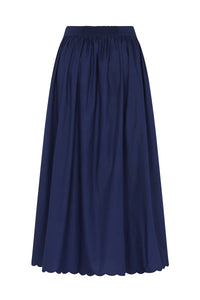 Back view of a navy blue midi skirt with a smocked elastic waistband, full gathered silhouette, and scalloped hem.