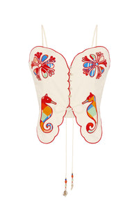 Off-white statement top featuring scalloped edges and vibrant embroidered appliqué details inspired by coastal motifs. Colorful seahorse designs, floral medallions, decorative buttons, and a front tie closure with beaded cord ends create a playful handcrafted look.