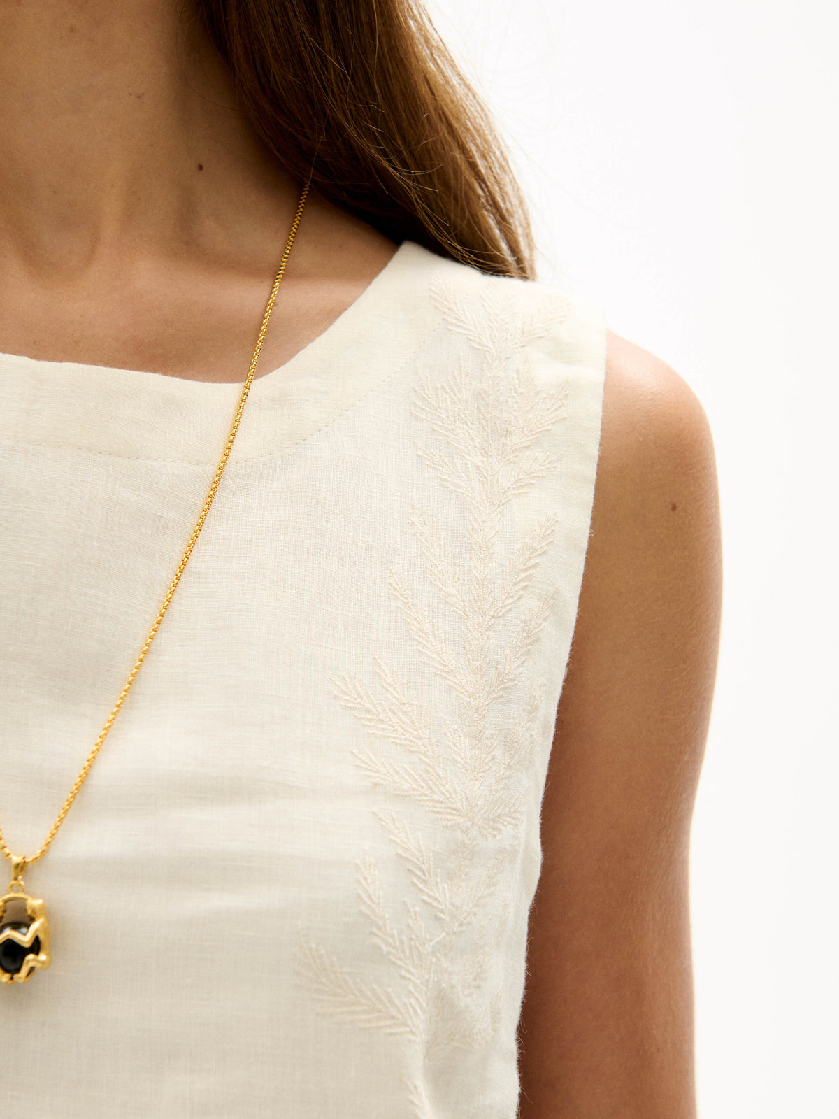 Close-up of cream sleeveless top with subtle tonal embroidery detail and smooth linen texture