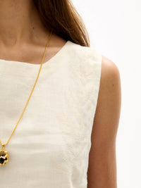 Close-up of cream sleeveless top with subtle tonal embroidery detail and smooth linen texture