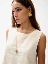 Close-up of cream embroidered sleeveless top with round neckline styled with gold pendant necklace and earrings