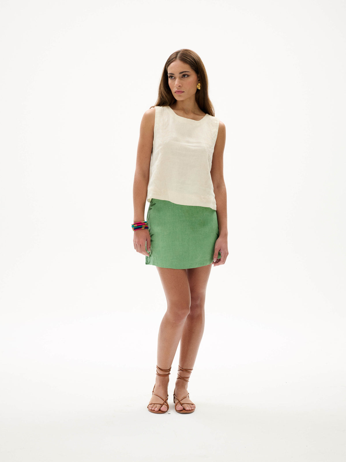 Model wearing cream embroidered sleeveless top and green mini skirt, styled with sandals, shown in angled view
