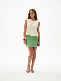Model wearing cream embroidered sleeveless top and green mini skirt, styled with sandals, shown in angled view