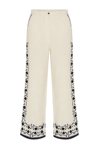 Front view of cream wide-leg pants with navy floral embroidery running down the side seams and along the hem.