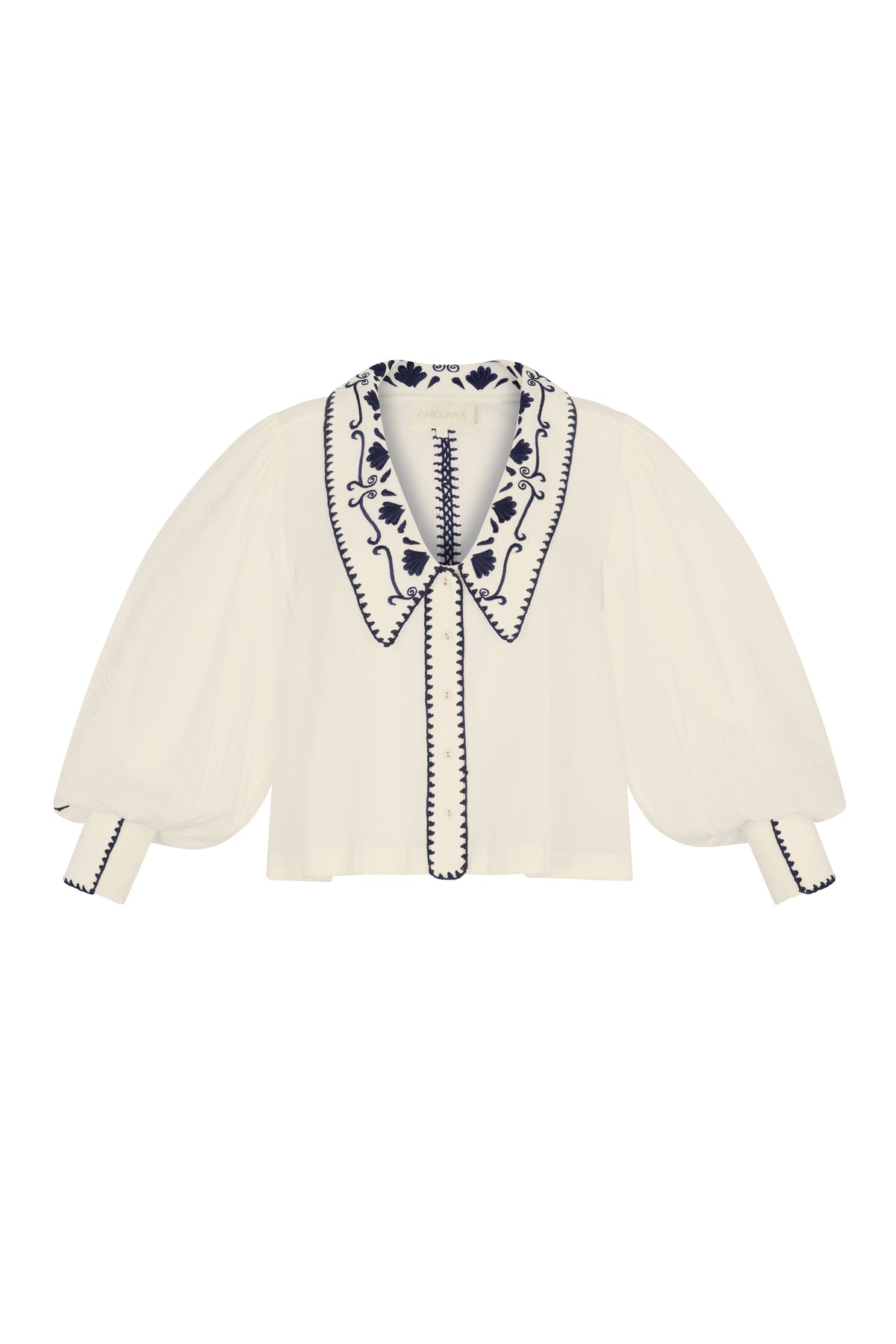 Front view of a cream blouse with a large embroidered collar, navy floral detailing, sheer puff sleeves, and embroidered trim along the button placket and cuffs.