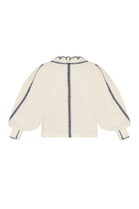 Back view of a cream blouse with voluminous sheer sleeves, navy embroidered trim along the sleeves and center back, and a wide embroidered collar.