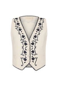 Front view of a cream sleeveless vest with a deep V-neck, front buttons, and navy floral embroidery along the neckline and front panels.
