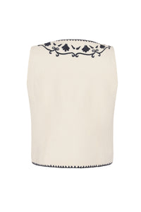 Back view of a cream sleeveless vest with navy embroidered detailing across the upper back and trim along the hem.