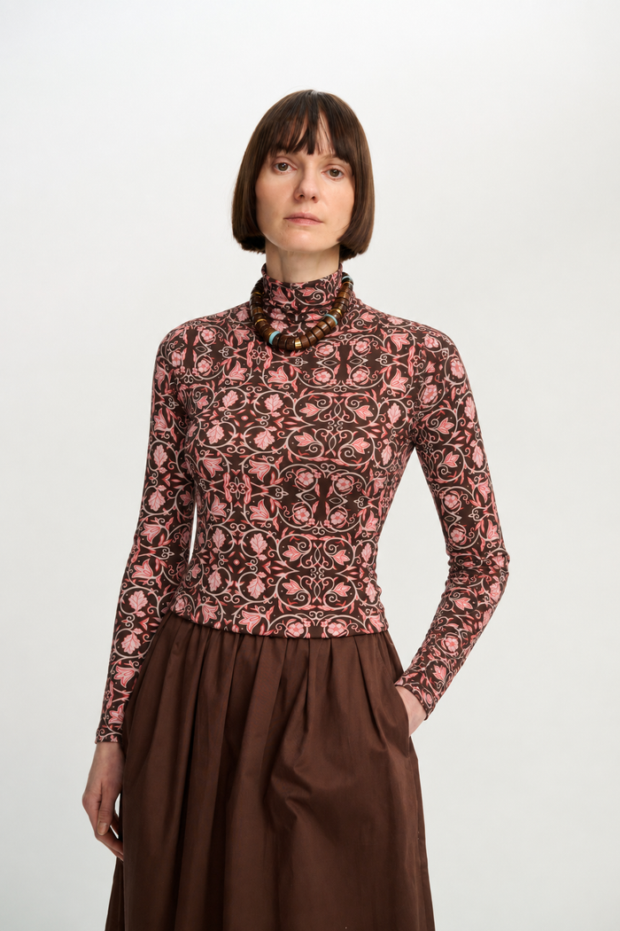 Front view of a model wearing the printed long-sleeve turtleneck with a brown skirt and statement beaded necklace.