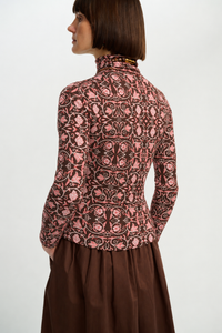 Back view of a model wearing the fitted chocolate-brown turtleneck with an all-over pink botanical print, styled with a brown skirt.